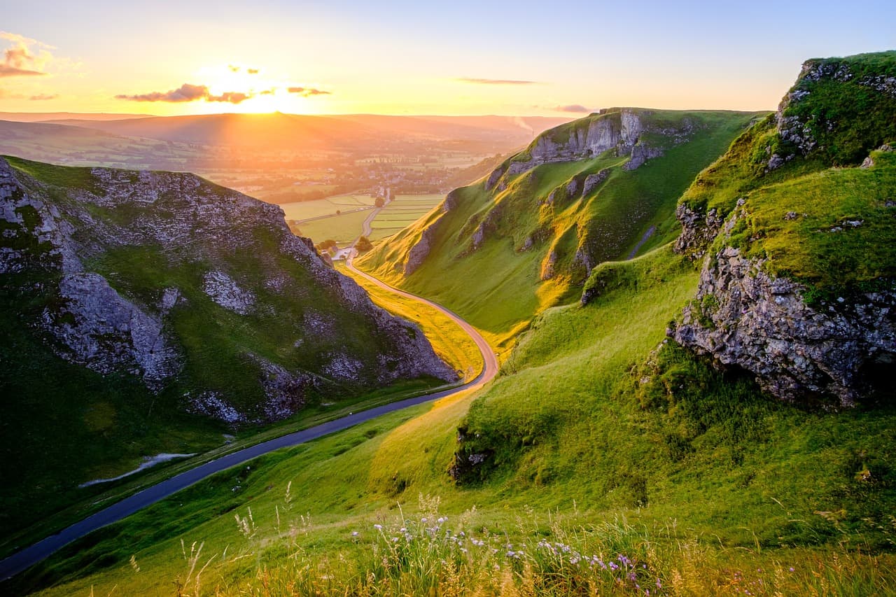 A road winding down through a steep green pass at sunset
